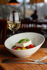 Traditional fresh greek salad with cherry tomatoes, bell pepper, cucumber and feta cheese dressed with olive oil served with white wine on wooden table with blurred background