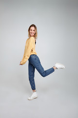 Feeling comfortable in her style. Full length studio shot of attractive young woman in casual wear smiling and looking away while jumping against grey background