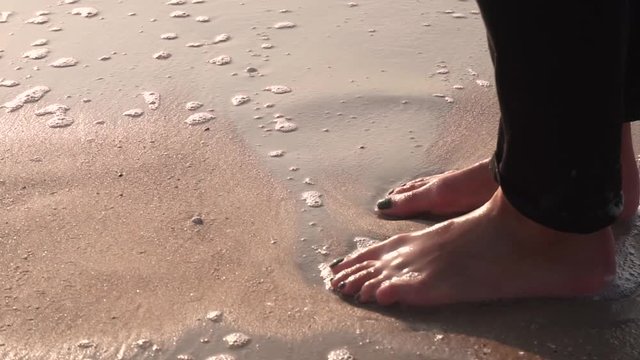Girl's legs in black jeans on the wet sand washes surf, wave with foam