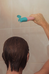 A woman in the shower pours shampoo on her head.