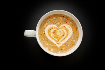 white wide cup of coffee with crema in the shape of a heart, cappuccino on a black background with vignette, top view, save space, close-up, love concept