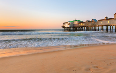 Naklejka premium Beautiful sunrise over Old Orchard Beach Pier, Saco Maine USA. The wooden pier on the beach contains many other tourist businesses, including a variety of souvenir shops.