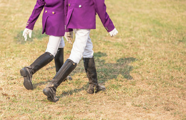 Fototapeta premium Young girl equestrians in professional apparel dressage purple jacket competition with black leather horseman boots walking in the field