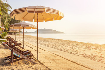 Row of empty wooden beach chairs with parasols on tropical sandy beach in the morning  relax leisure summer holidays concept 