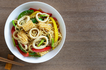 top view of stir fried japanese noodles with squid and sweet pepper in a ceramic plate on wooden table. asian homemade style food concept.