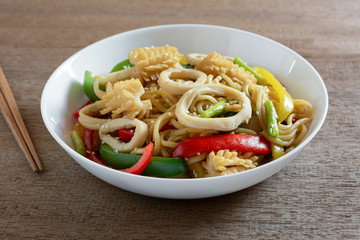 stir fried japanese noodles with squid and sweet pepper in a ceramic plate on wooden table, close up. asian homemade style food concept.