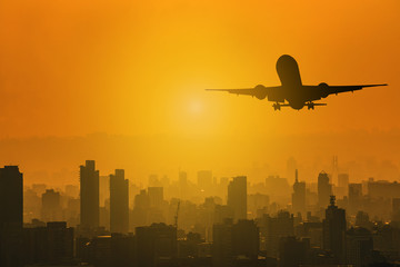 Silhouette of commercial plane flying over a city during with skylight sunset with copy space for...