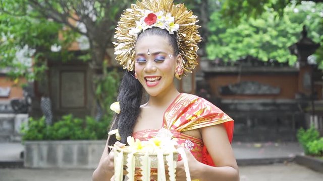 Beautiful balinese dancer standing in a temple while smiling and holding frangipani flower
