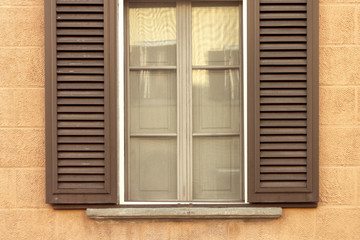 brown wooden window with shutters on yellow textural wall