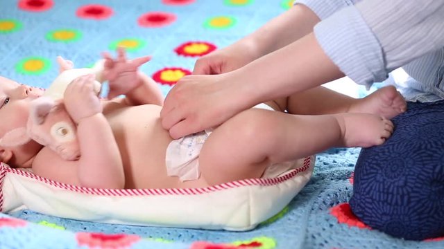The mother changes the diaper for her newborn baby in the nursery. Newborn care, diaper change, healthy baby.