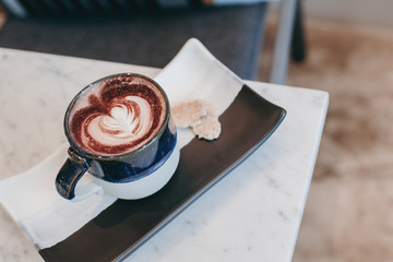Coffee in blue cup on wooden table in cafe with lighting background