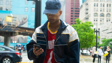 Chicago, IL/United States-June 12th 2019:  Young attractive Middle eastern male model is talking on his smart phone smiling while wearing fashion trendy clothes. view from a inside a window pane