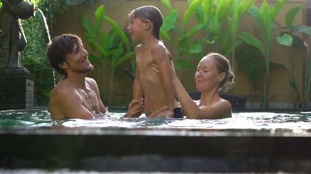 Happy family - father mother and son have fun in their swimming pool