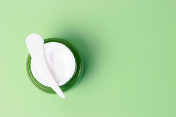 Green jar with white cream and plastic spatula on background, top view, copy space