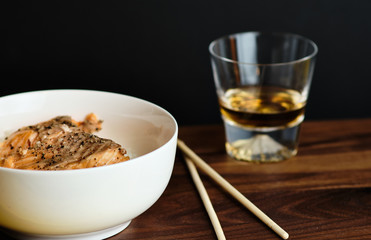 Salmon on a bed of rice next to chopsticks and glass of whiskey
