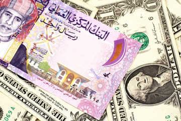 A close up image of a colorful one rial bank note from Oman on a bed of American one dollar bills in macro