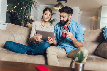 Smiling couple using digital tablet and credit card at home
