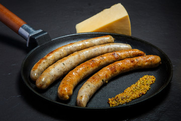 closeup frying pan with fried thin sausages and granular mustard