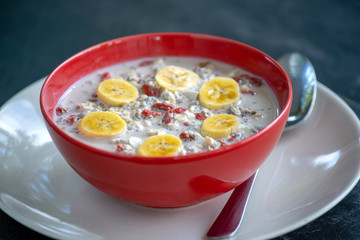 Fresh breakfast of granola, yogurt, nuts, goji berries, chia seeds and banana. Muesli with fruits and berries in red bowl