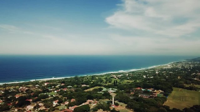 Aerial footage filmed by a Drone of Scottburgh Beach and Land grassy fields with residential houses overlooking the sea in Kwa Zulu Natal South Africa