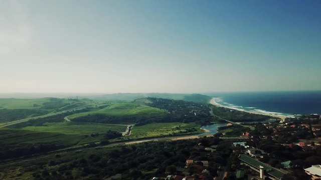 Aerial footage filmed by a Drone of Scottburgh Beach and Land grassy fields with residential houses overlooking the sea in Kwa Zulu Natal South Africa