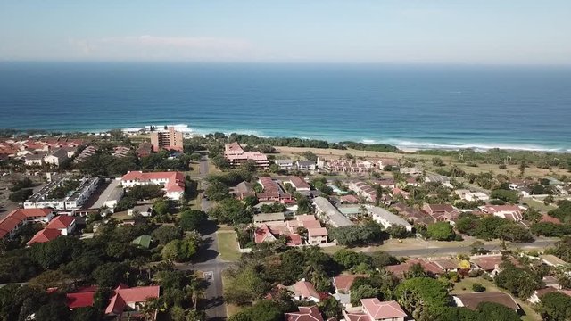 Aerial footage filmed by a Drone of Scottburgh Beach and Land grassy fields with residential houses overlooking the sea in Kwa Zulu Natal South Africa