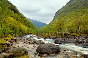 Spring mountain landscape Norway, Stormy river flows among stone boulders, hills and forests