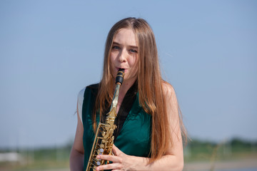 Beautiful brunette plays the saxophone in the park