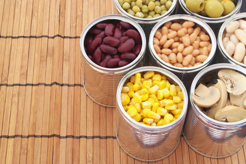 Preserved food on bamboo mat background.Canned green peas, beans, corn, olives and mushrooms in tin cans. 