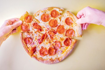 Pepperoni pizza on a yellow background. Hands take pieces of pizza. Concept of italian food, fast food, unhealthy food. Salami, cheese. Bright image, minimalism, top view, flat lay. Place for text.
