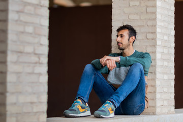 Portrait of a young man with beard and casual clothes sitting in an urban park
