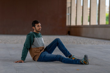 Portrait of a young man with beard and casual clothes sitting in an urban park