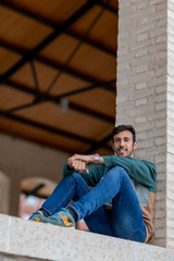 Portrait of a young man with beard and casual clothes sitting in an urban park