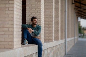 Portrait of a young man with beard and casual clothes sitting in an urban park