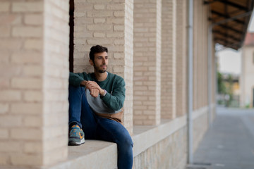 Portrait of a young man with beard and casual clothes sitting in an urban park