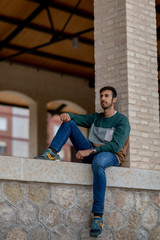 Portrait of a young man with beard and casual clothes sitting in an urban park