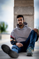 Portrait of a young man with beard and casual clothes sitting in an urban park