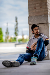 Portrait of a young man with beard and casual clothes sitting in an urban park