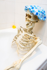 Bony skeleton taking a bubble bath in a grungy off-white dirty tub