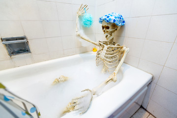 Bony skeleton taking a bubble bath in a grungy off-white dirty tub
