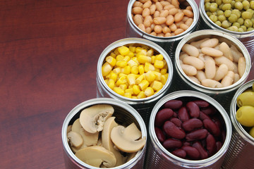 Canned green peas, beans, corn, and mushrooms in tin cans. Preserved food on wooden table with space for text