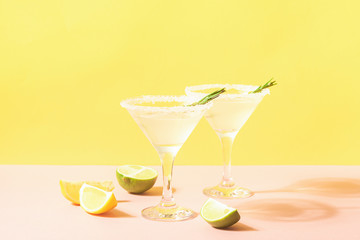 A drink of lemon and lime in elegant glasses pastel colored background with bright sunshine. Summer lemonade or mojito.