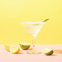 A drink of lemon and lime in an elegant glass pastel colored background with bright sunshine. Summer cocktail or mojito.