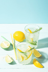 A drink of lemon and lime in an elegant glass on a blue background with bright sunshine. Summer cocktail or mojito.