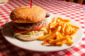 Tasty burger in the restaurant. Sesame bun, meat Patty, tomato, lettuce and pickle. Served with French fries