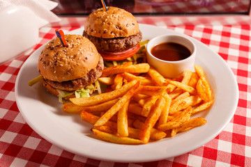 Two mini burgers in the restaurant. Sesame bun, meat Patty, tomato, lettuce and pickle. Tasty Served with French fries