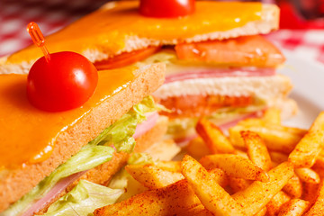 Close up Tasty grilled sandwich in the restaurant. Club sandwich with ham, tomato, cheese and lettuce. Served with French fries