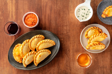 Empanadas with sauces and wine, shot from the top on a dark rustic wooden background with a place...