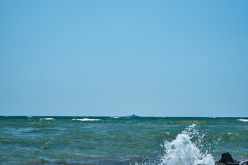 Image of the sea shore. In the background is a warship.