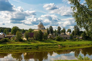 Fototapeta na wymiar View of the left bank of the river Msta and the Church of the Assumption of the Blessed Virgin Mary on a summer day